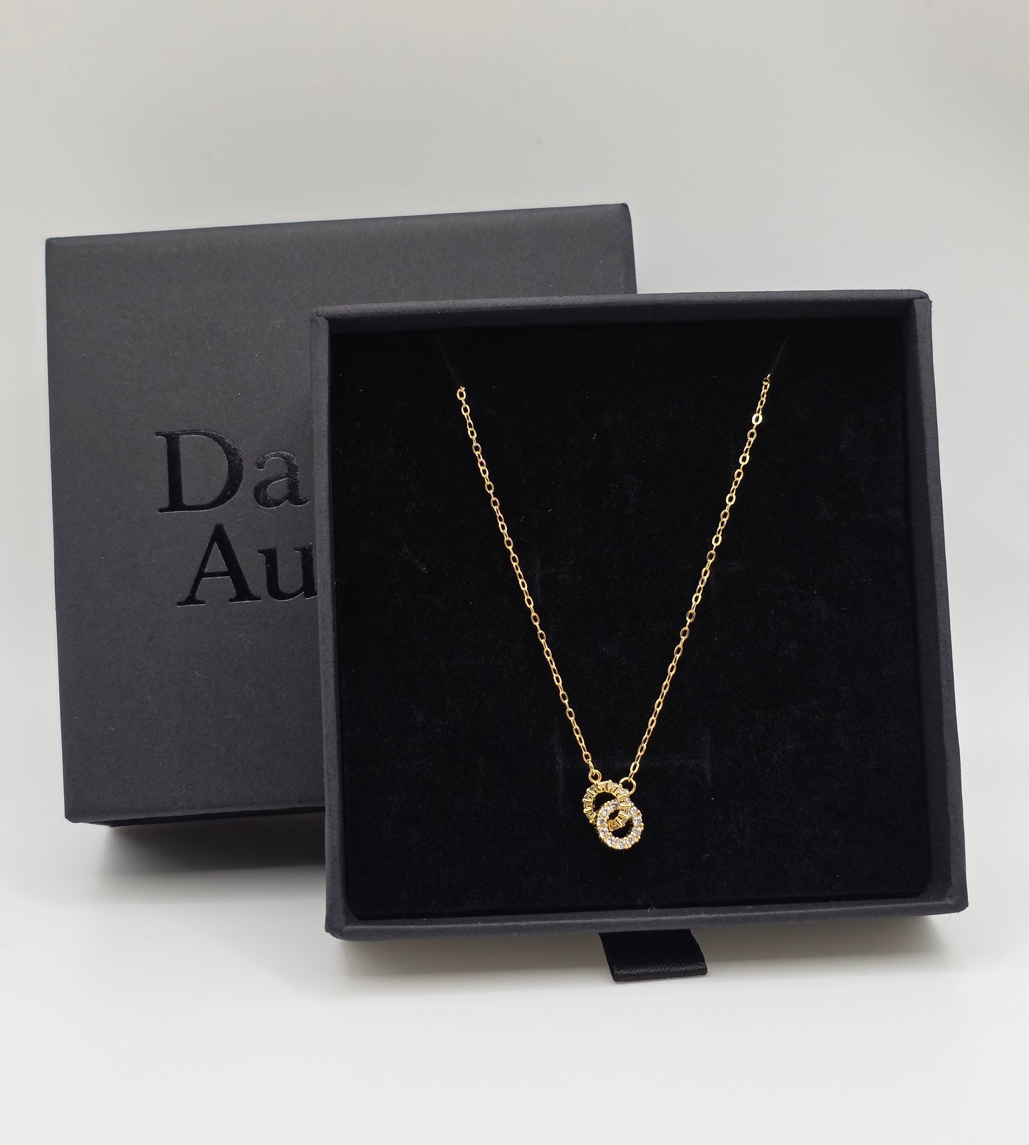 Gold necklace in a black box with 'Da naVi Aurum' branding on a white background