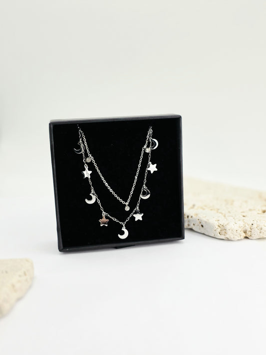 Silver necklace with star and moon charms on a black display stand against a white background