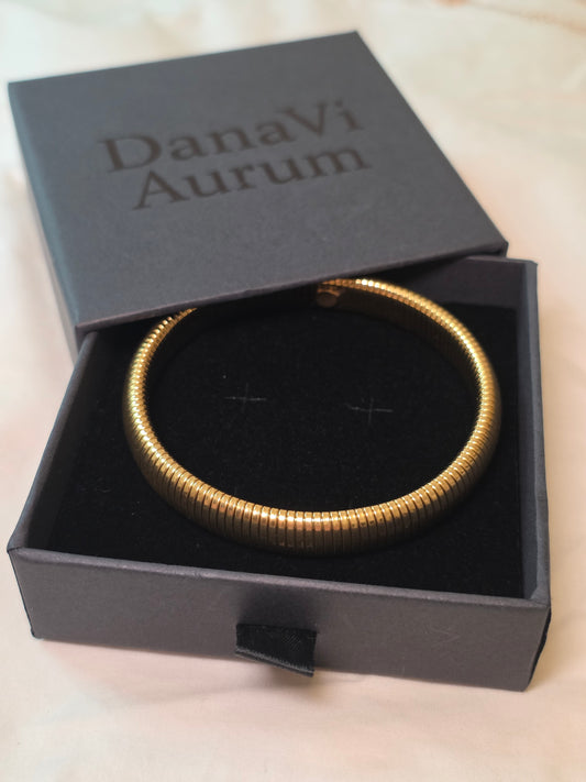 Gold bracelet in a black 'DanaVi Aurum' box on a beige background