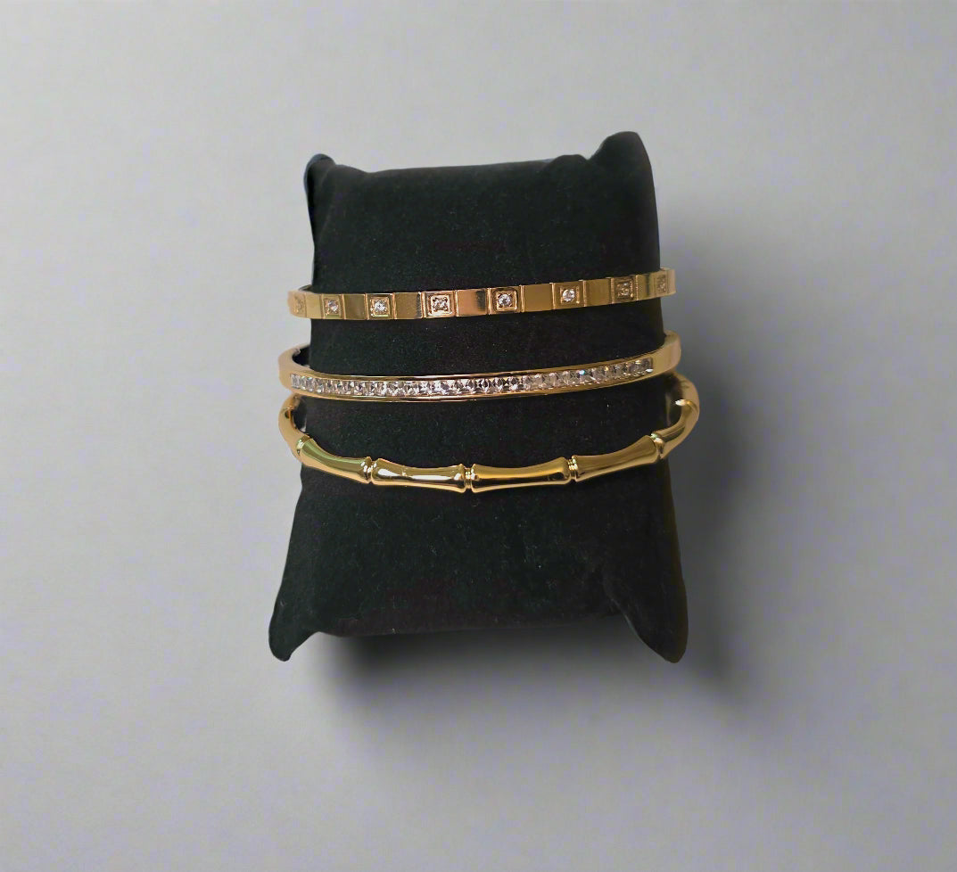 Set of gold bangles on a black jewelry pillow against a light pink background