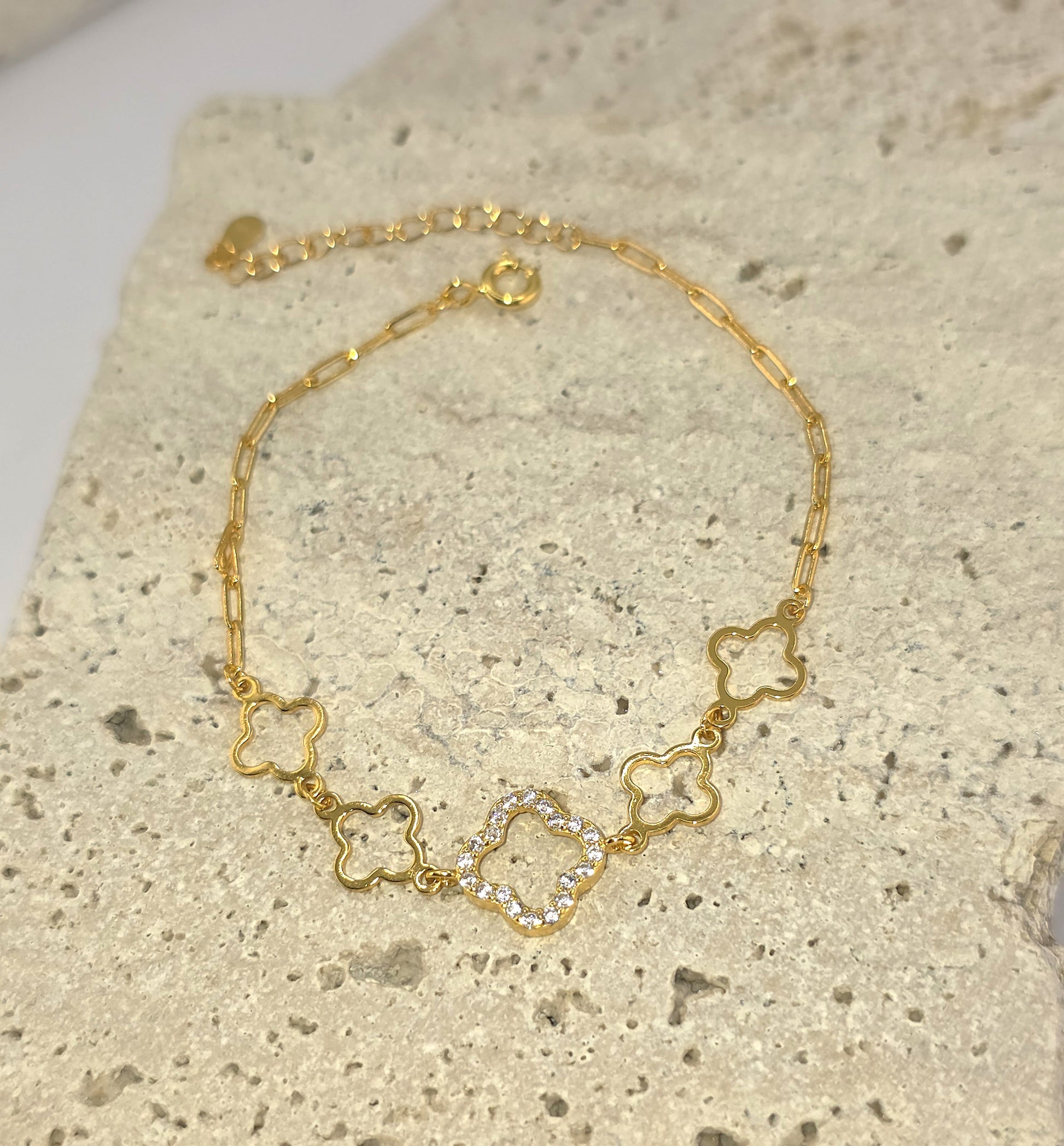 Gold necklace with clover-shaped links on a textured surface danavi aurum