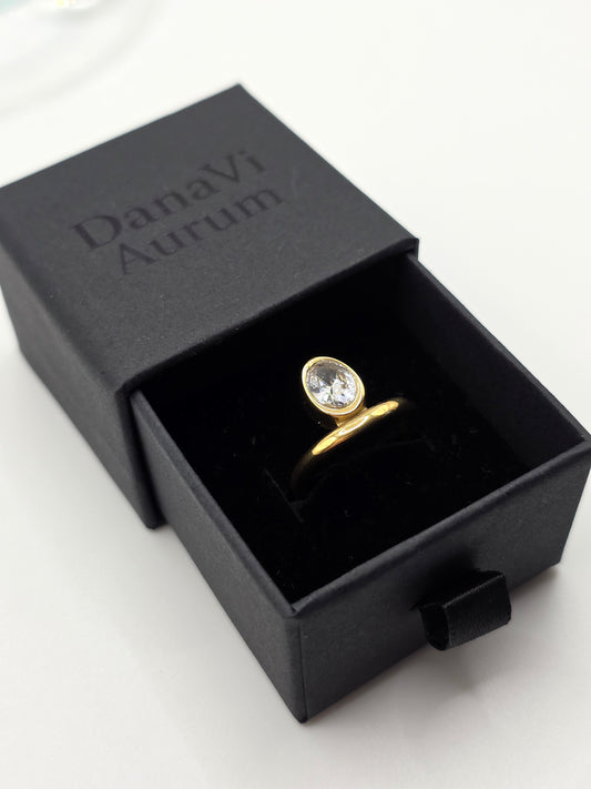 Gold ring with a diamond in a black 'Danavi aurum' box on a white background