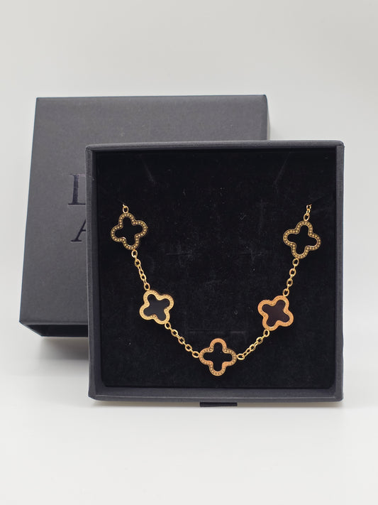 Gold bracelet with clover-shaped links in a black danavi aurum jewelry box on a light gray background