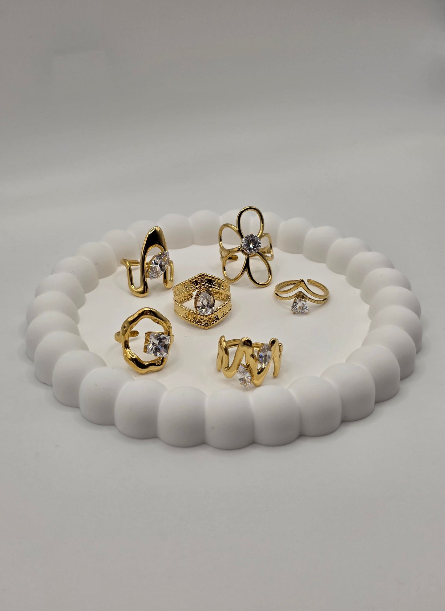 Set of gold and silver rings on a white shell-shaped stand against a light gray background Danavi Aurum