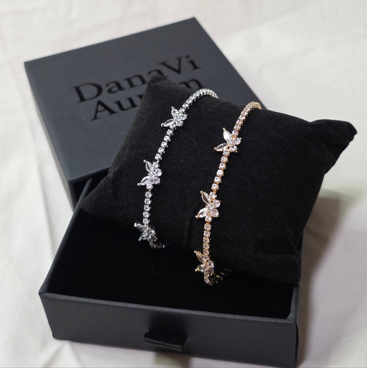 Two butterfly-themed bracelets on a black box with 'Danavi Aurum' branding.