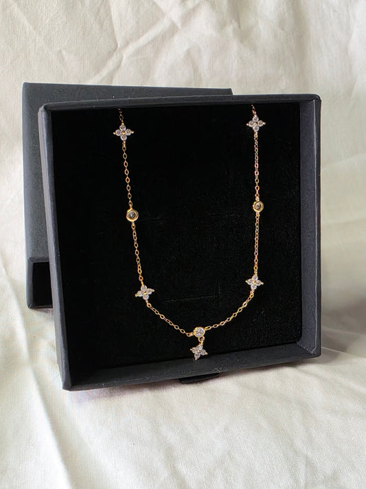 Gold necklace with star-shaped charms in a black Danavi Aurum box on a white fabric background