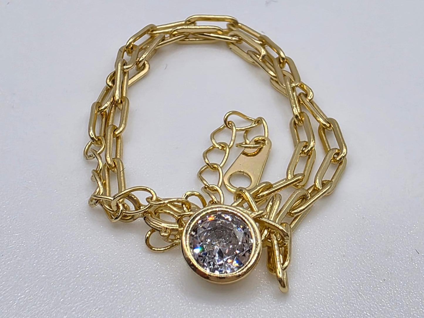 Gold chain bracelet with a central gemstone charm on a light gray background