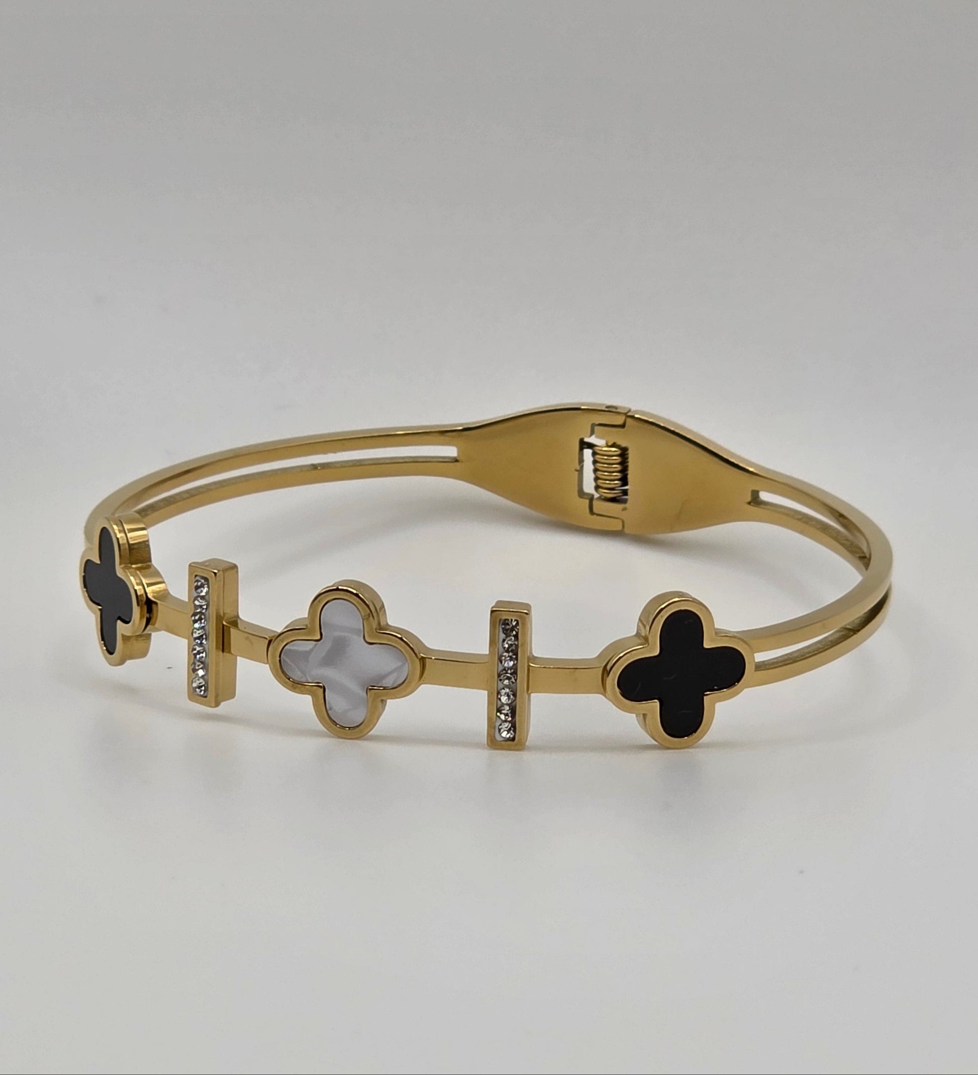 Gold bracelet with black and white clover-like charms on a light gray background danavi aurum