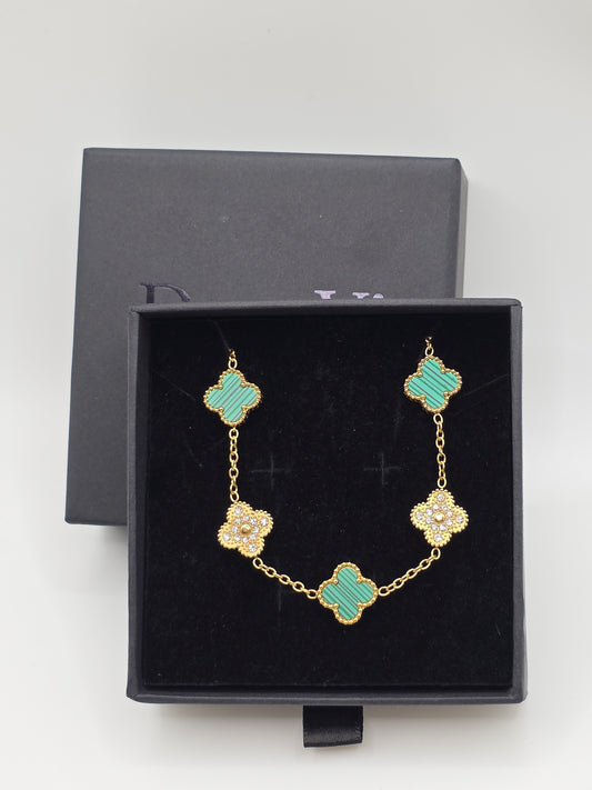 Gold bracelet with green clover-shaped stones in a black Danavi Aurum jewelry box on a light gray background