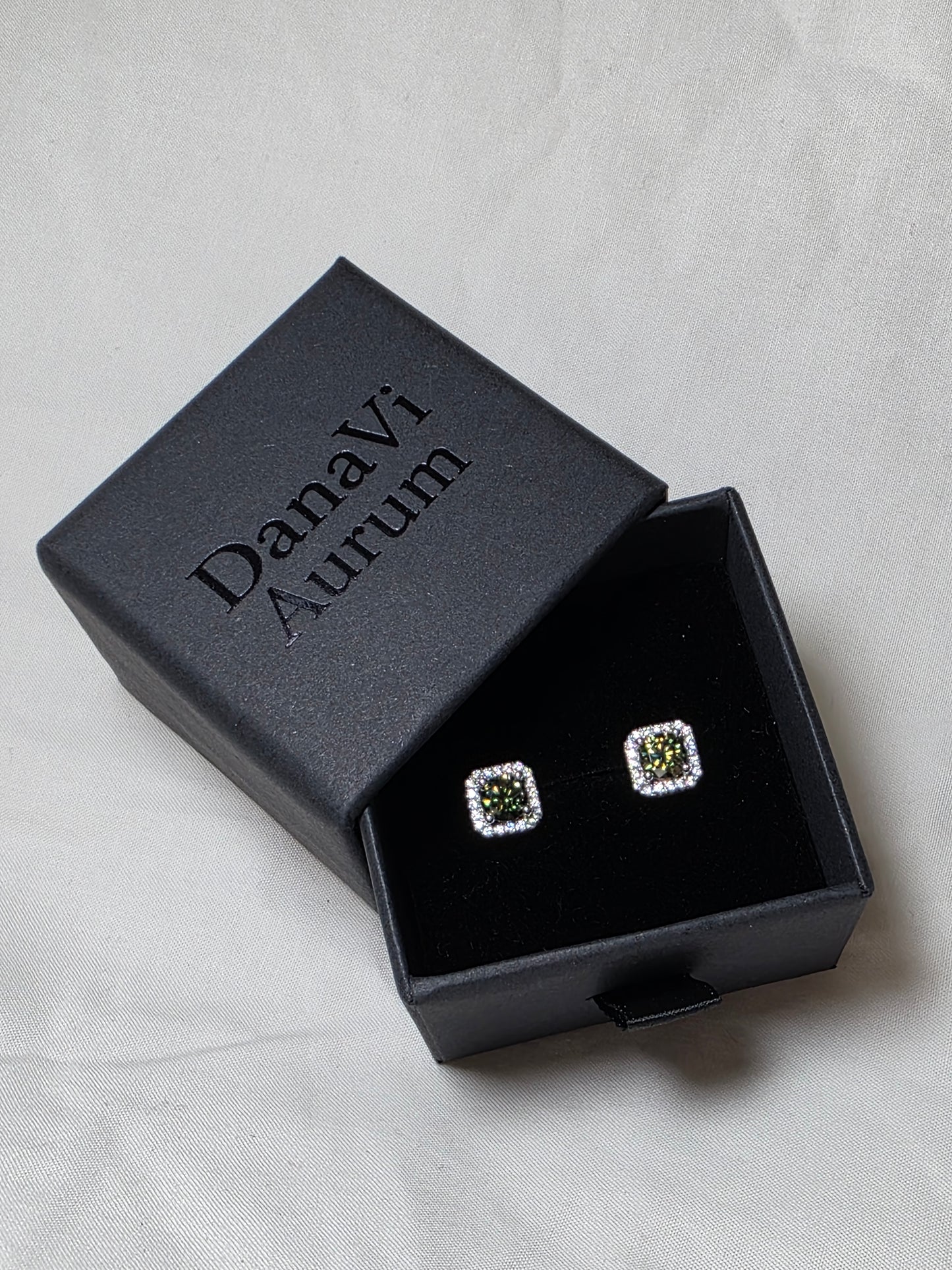 Square earrings with emerald like gemstones in a black jewelry box on a light gray background