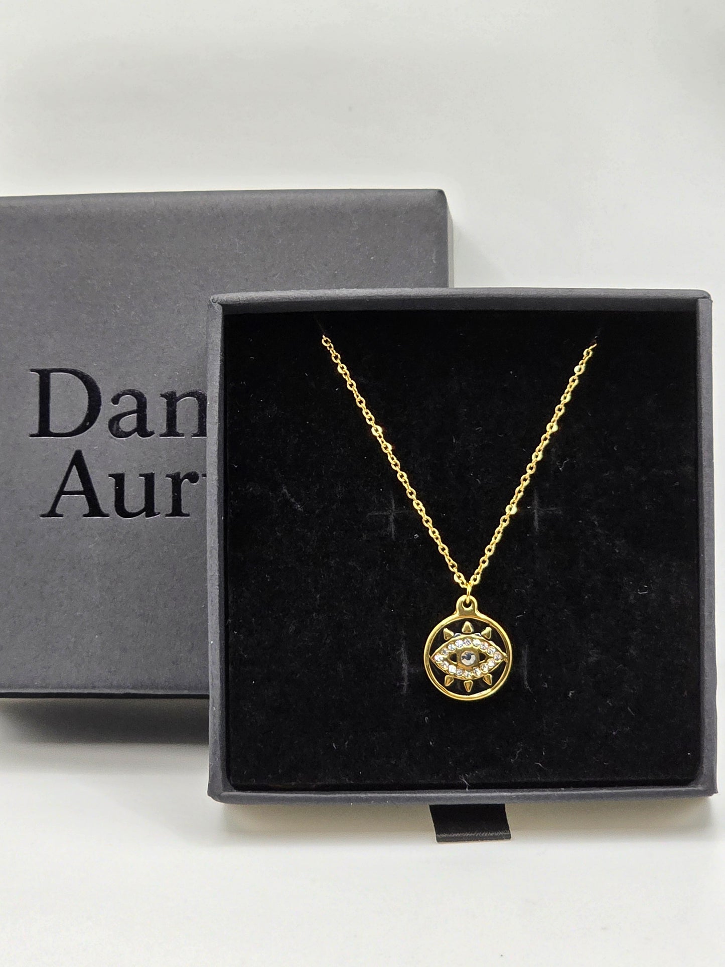 Gold necklace with a pendant in a black box labeled 'Danavi Aurum' on a light gray background