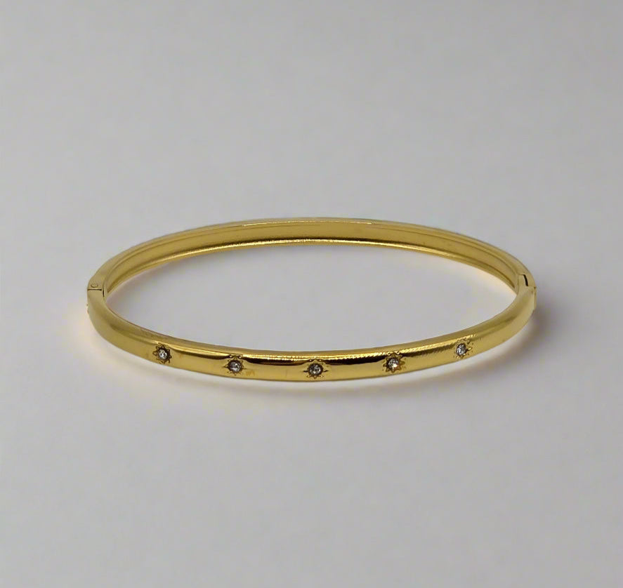 Gold bangle with small stones on a light gray background