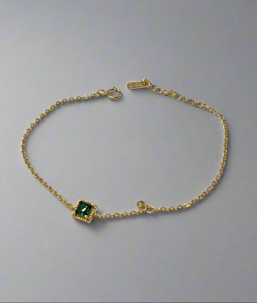 Gold bracelet with a green gemstone on a textured gray background danavi aurum