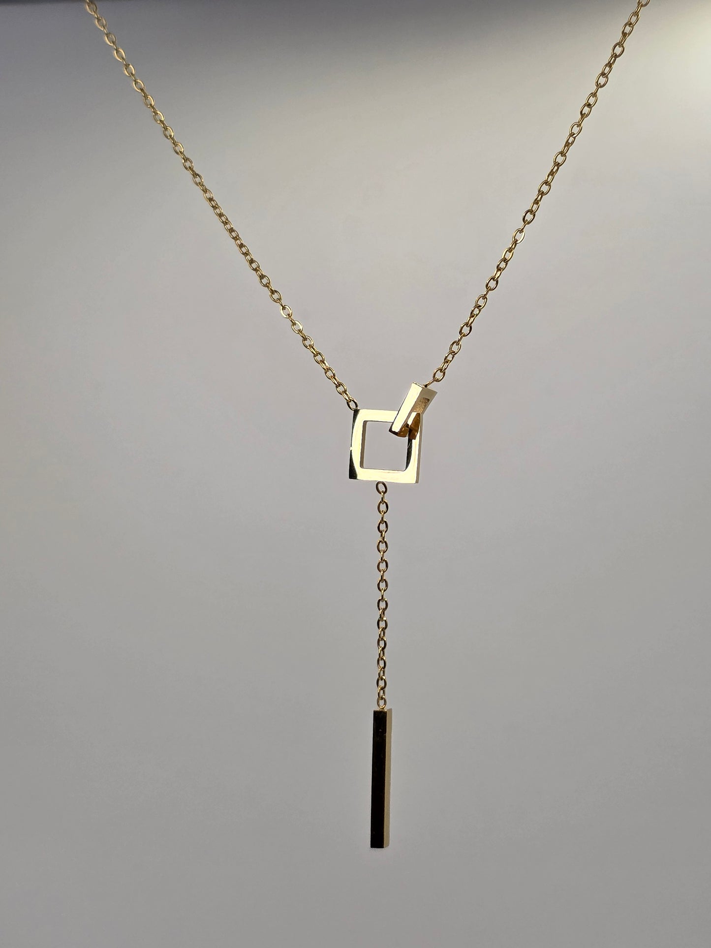 Gold necklace with a square pendant on a gray background danavi aurum