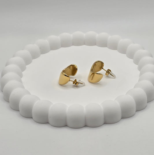 Gold heart-shaped earrings on a white beaded stand against a light gray background danavi aurum