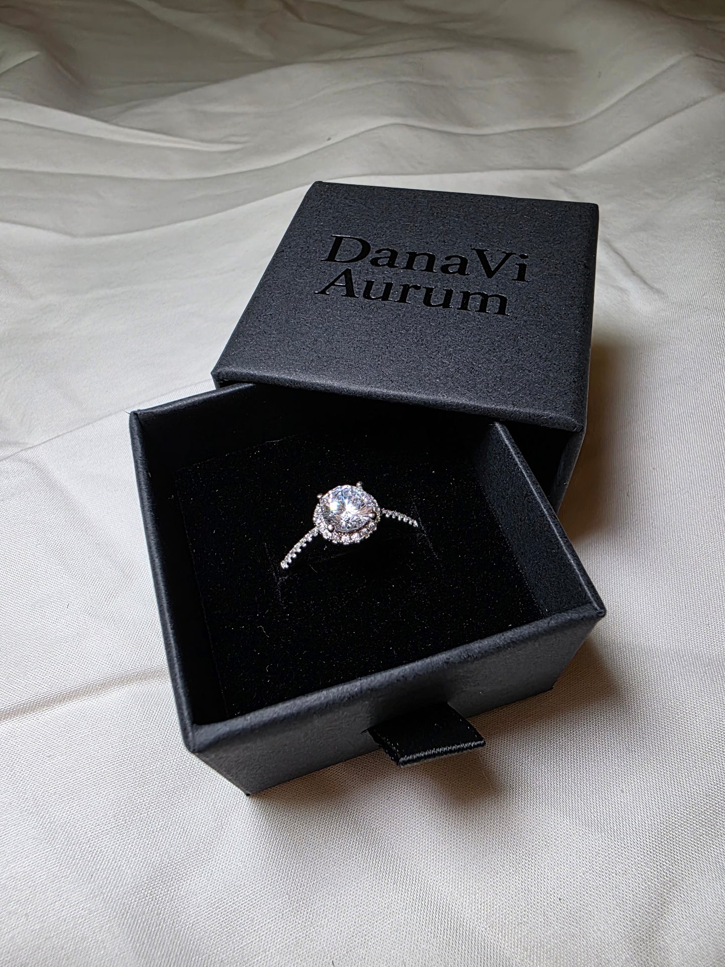 Silver ring in a black 'Danavi Aurum' box on a white fabric background