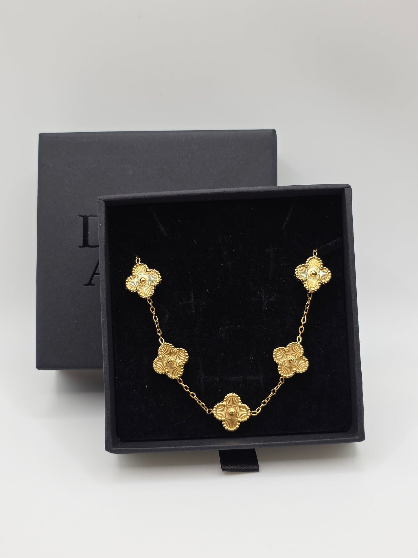 Gold bracelet with floral designs in a black jewelry box on a light gray background danavi aurum