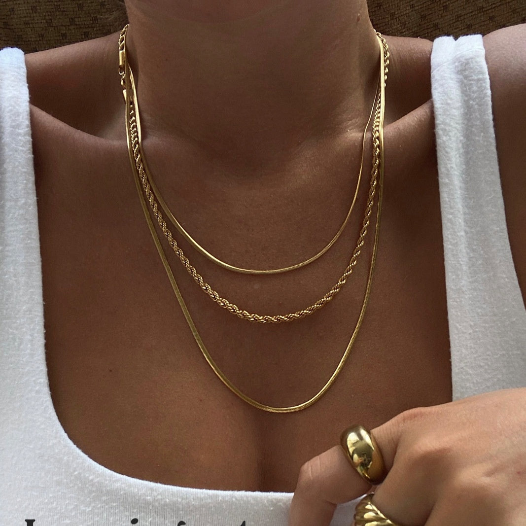 Gold necklace and ring on a person wearing a white top.