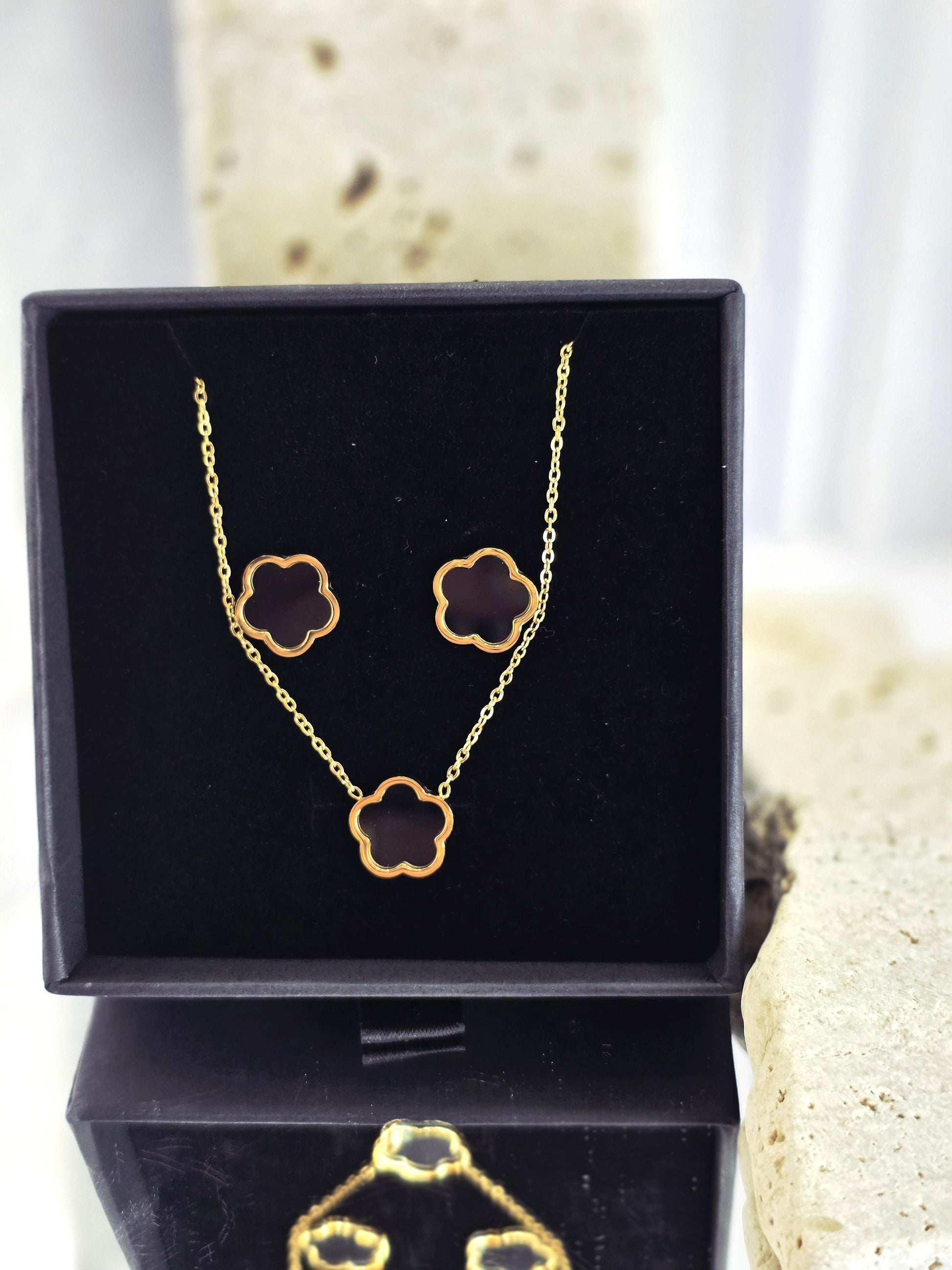 Gold necklace and earrings set in a black box on a textured surface