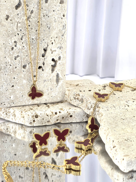 Butterfly-themed jewelry set including necklace, earrings, and bracelet on a stone surface.