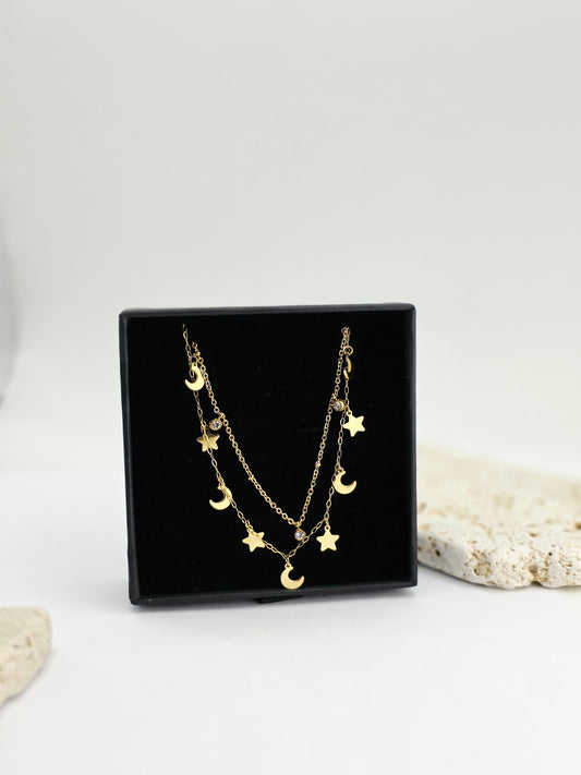 Gold necklace with star and moon charms on a black display box against a white background danavi aurum