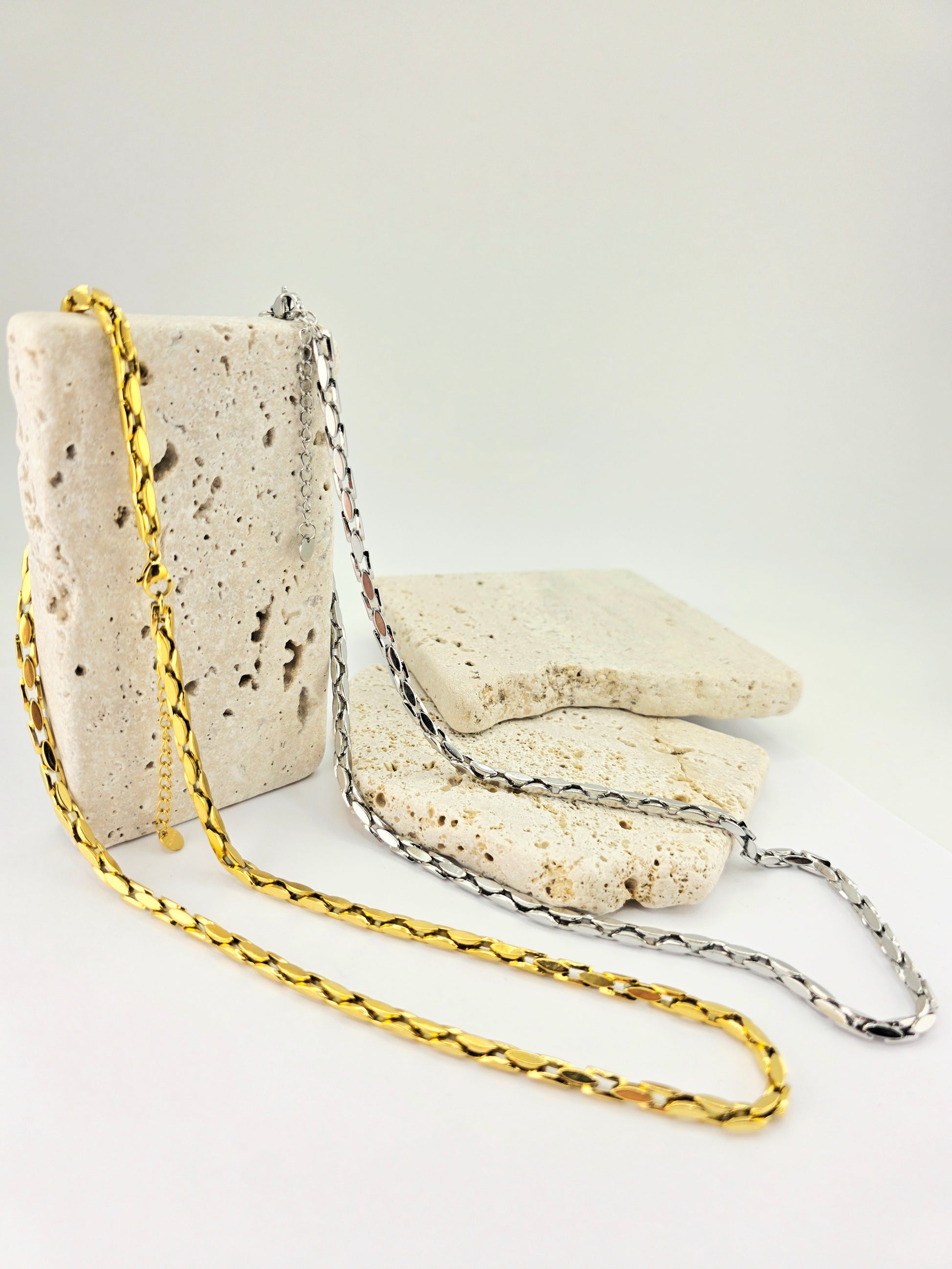 Two gold chains on a textured stone surface with a white background