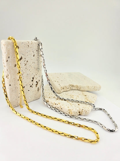 Two gold chains on a textured stone surface with a white background