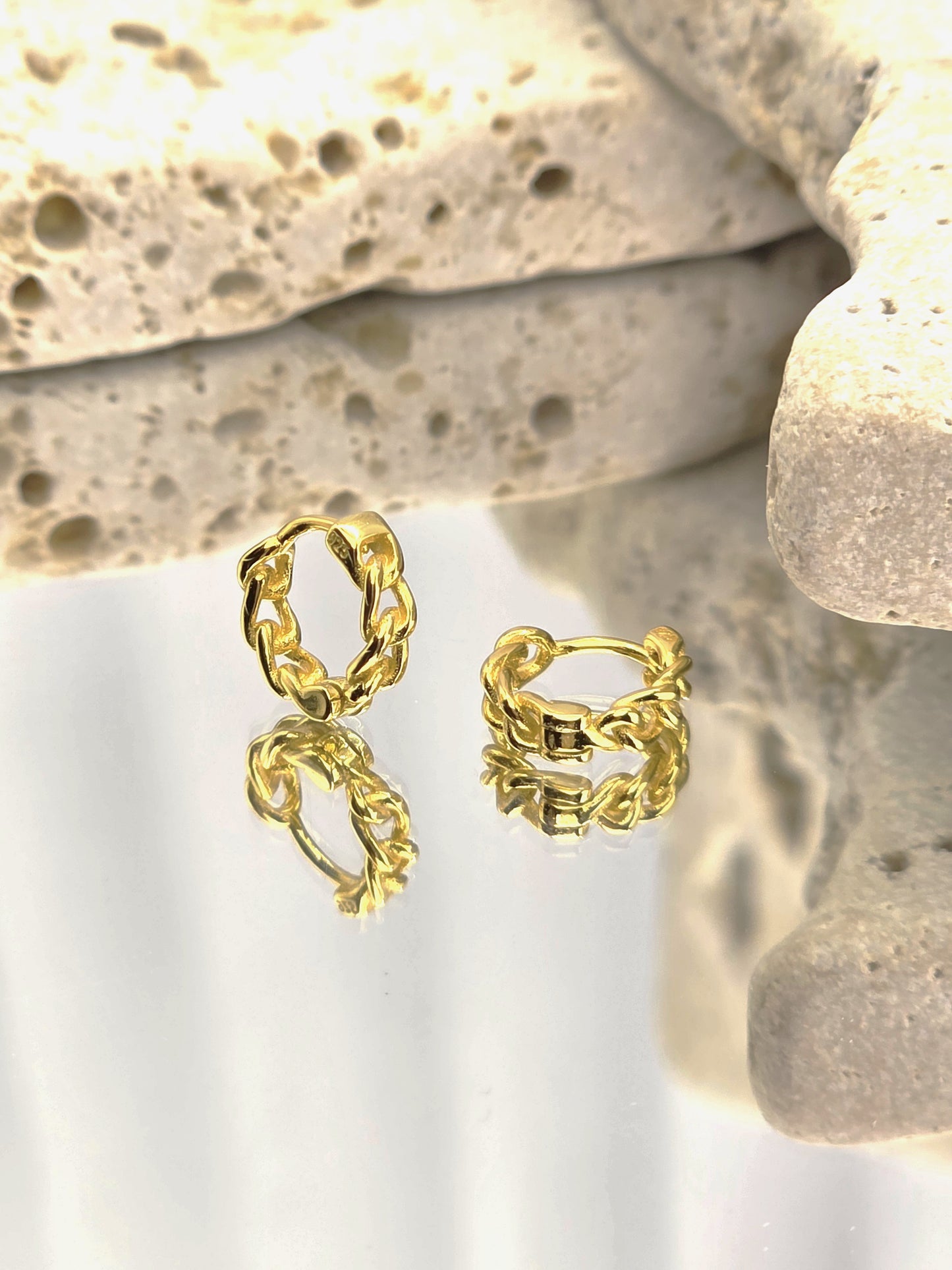 Gold hoop earrings on a reflective surface with a stone background