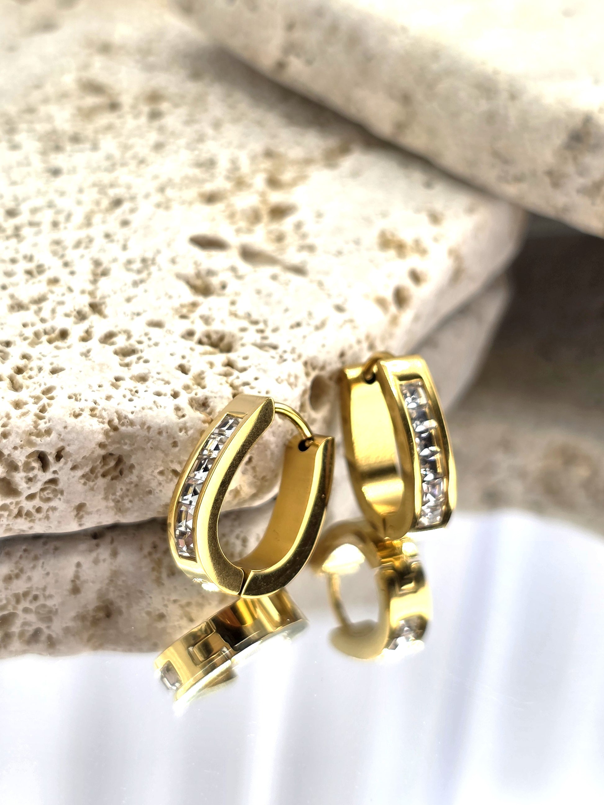 Gold hoop earrings with embedded stones on a textured stone surface DanaVi Aurum