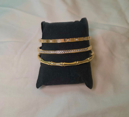 Set of gold bangles on a black jewelry pillow against a light pink background
