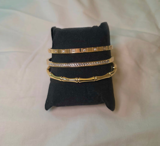 Set of gold bangles on a black jewelry pillow against a light pink background