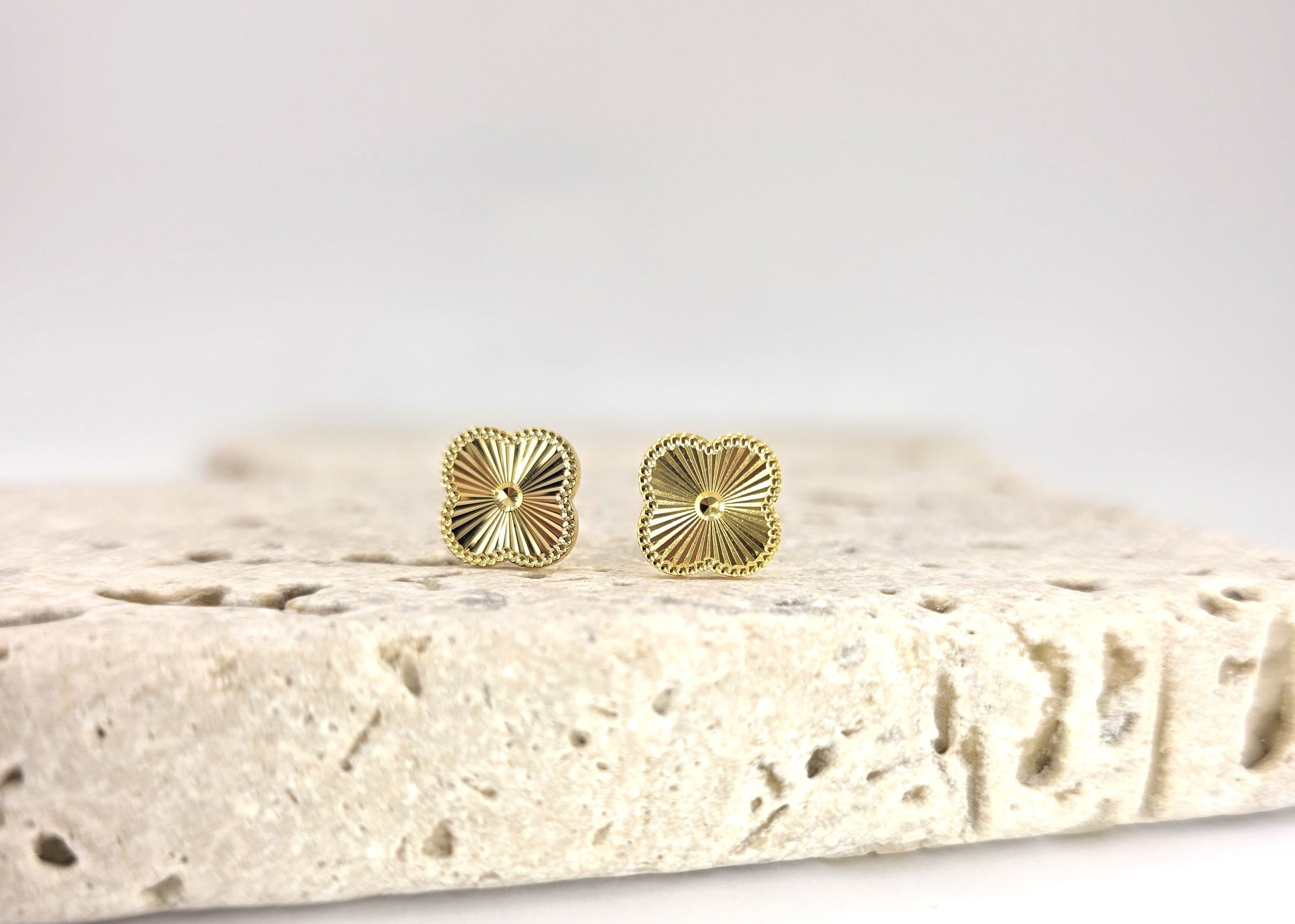 Gold stud earrings on a textured stone surface with a light gray background