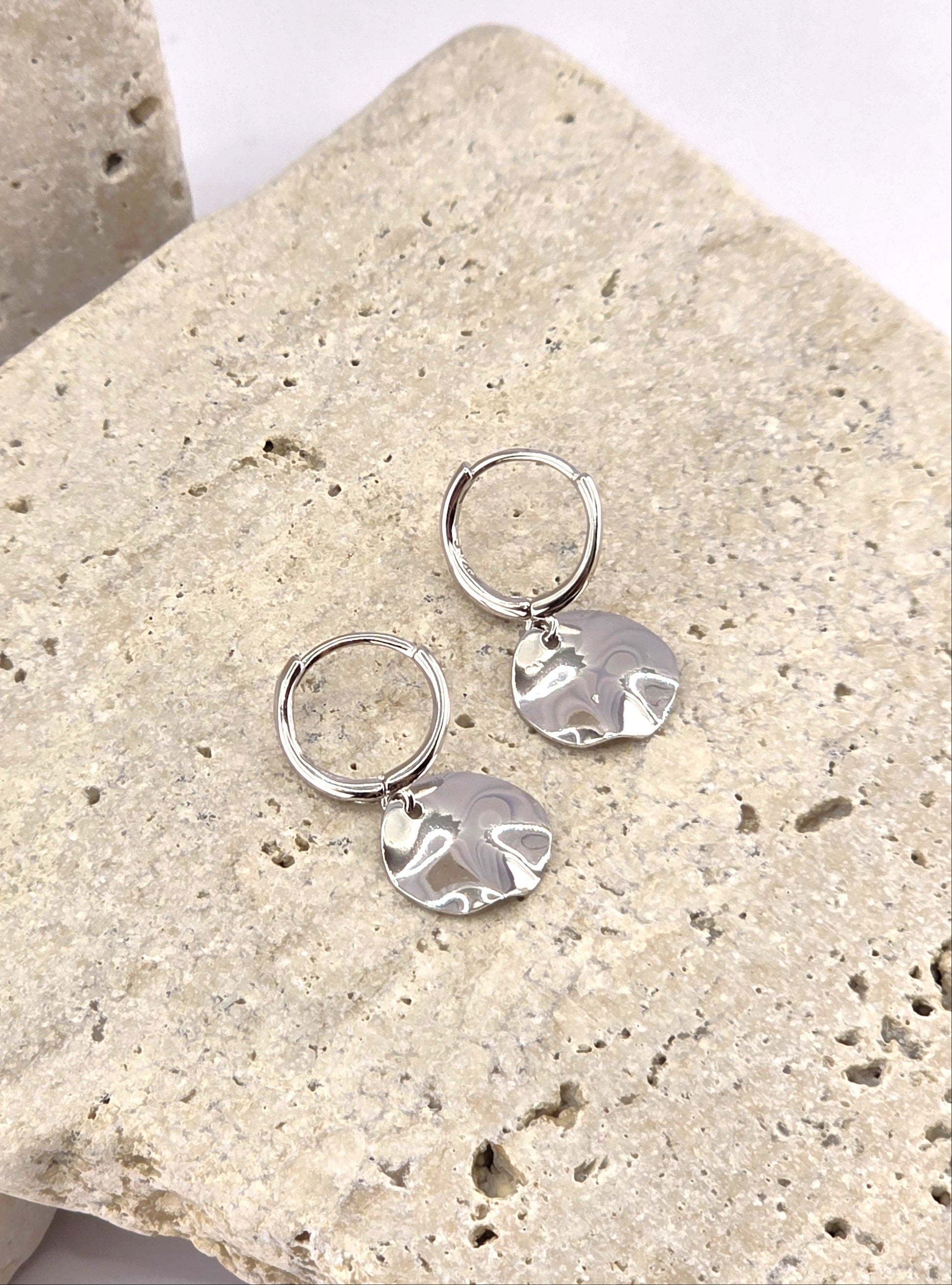 Silver earrings on a textured stone surface