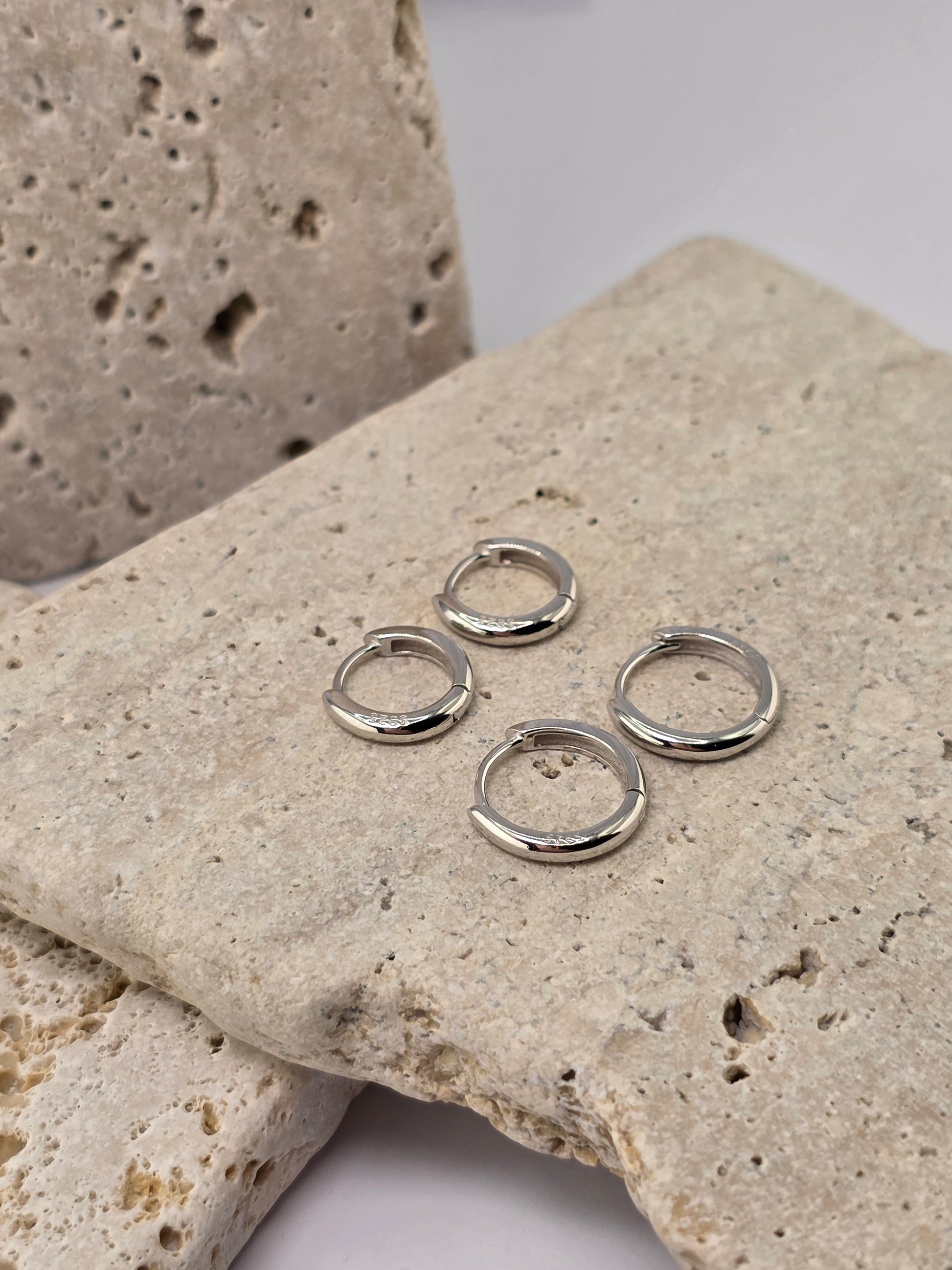 Silver hoop earrings on a textured stone surface