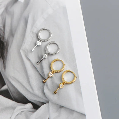Pair of gold and silver key-shaped earrings on a light fabric background danavi aurum