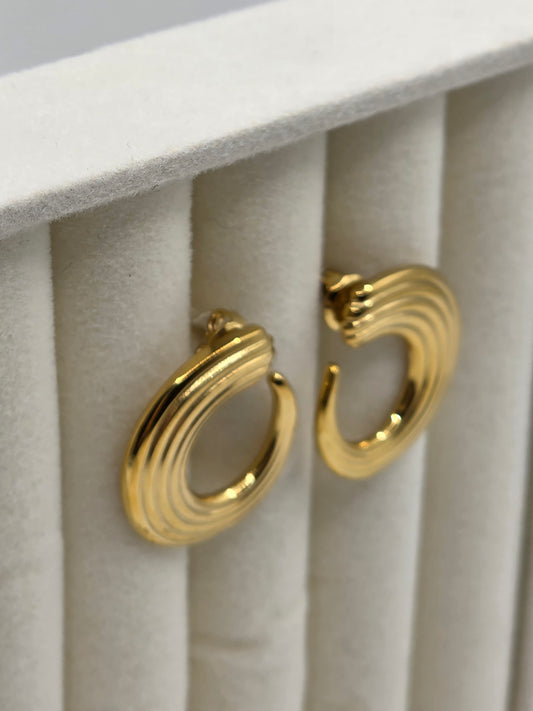 Gold hoop earrings on a soft white surface danavi aurum