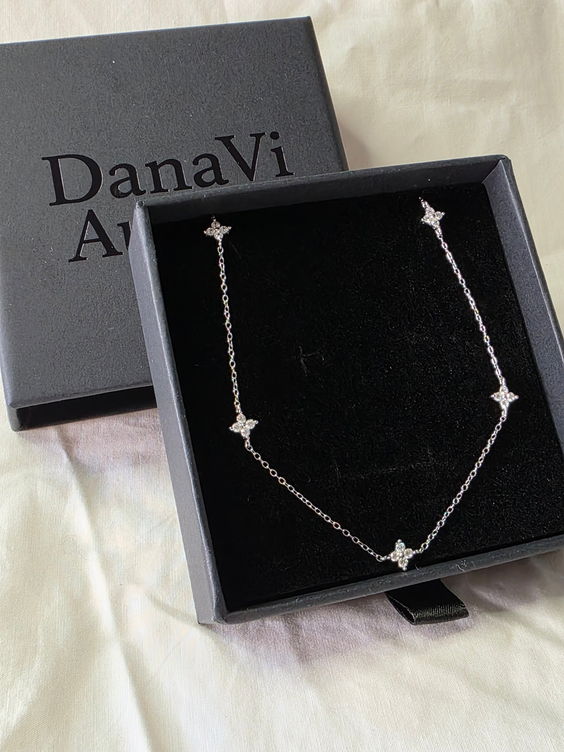 Silver necklace with star details in a black box labeled 'DanaVi Aurum' on a white fabric background