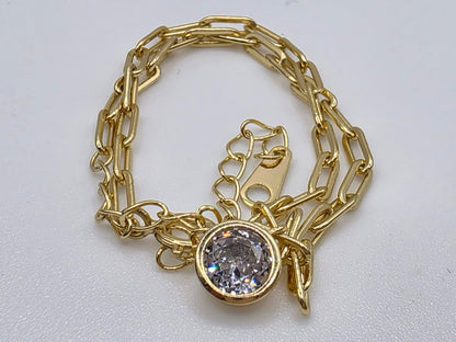 Gold chain bracelet with a central gemstone charm on a light gray background