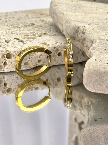 Gold hoop earrings with small diamonds on a textured stone surface danavi aurum