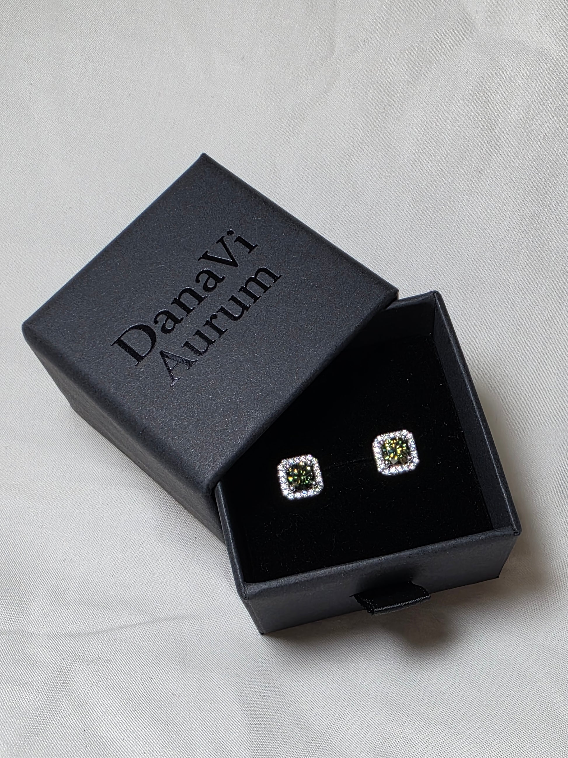 Square earrings with emerald like gemstones in a black jewelry box on a light gray background