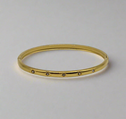 Gold bangle with small stones on a light gray background