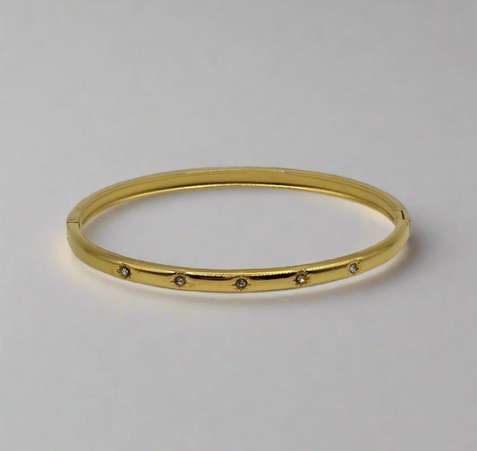 Gold bangle with small stones on a light gray background