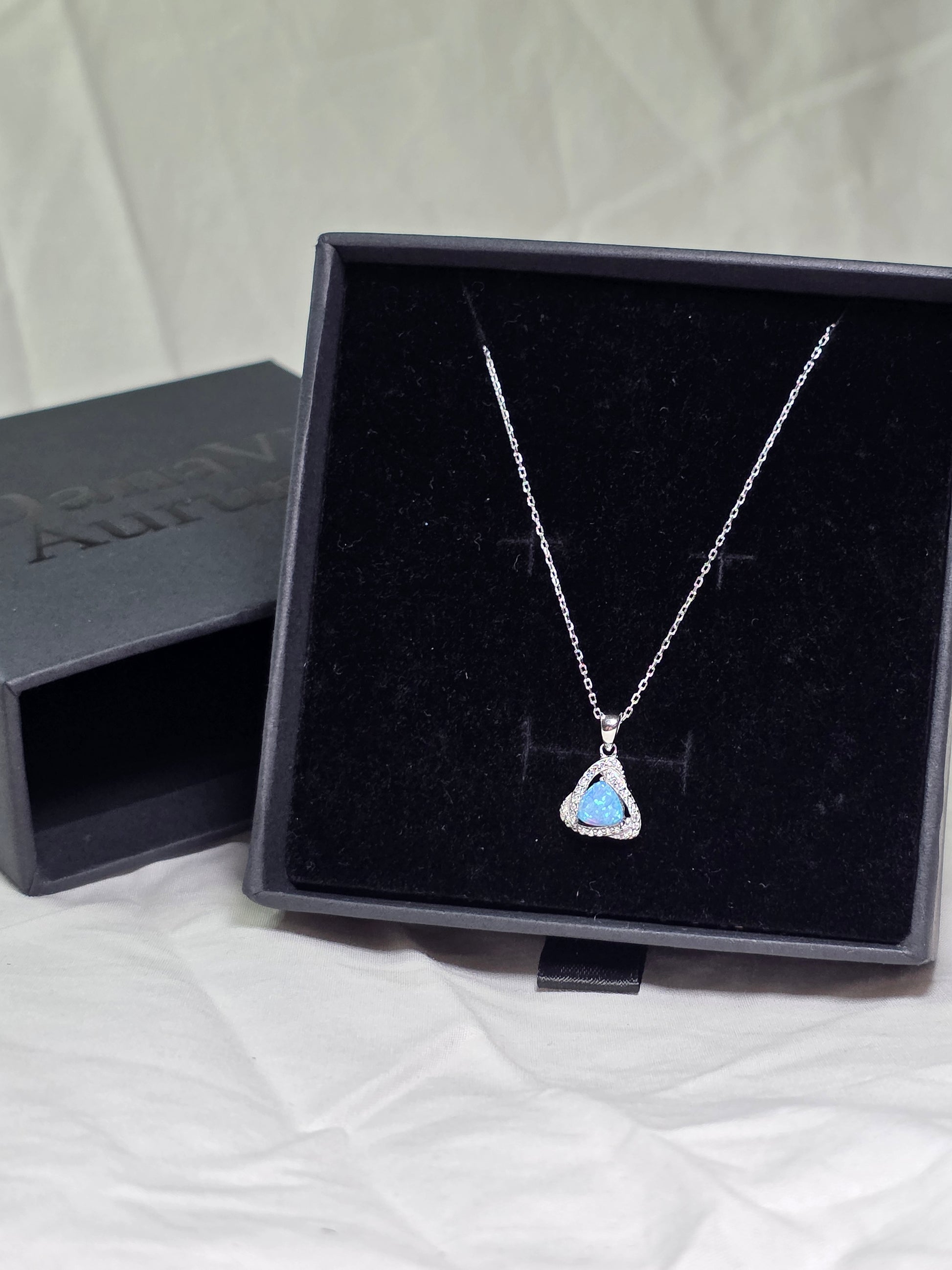 Necklace with a heart-shaped blue pendant in a black Danavi Aurum jewelry box on a white surface
