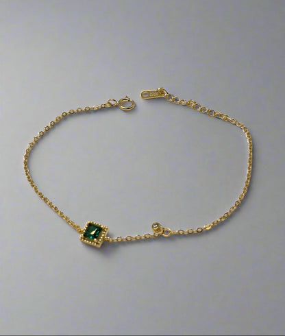 Gold bracelet with a green gemstone on a textured gray background danavi aurum