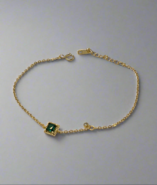 Gold bracelet with a green gemstone on a textured gray background danavi aurum