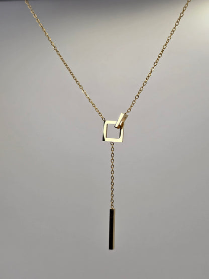 Gold necklace with a square pendant on a gray background danavi aurum