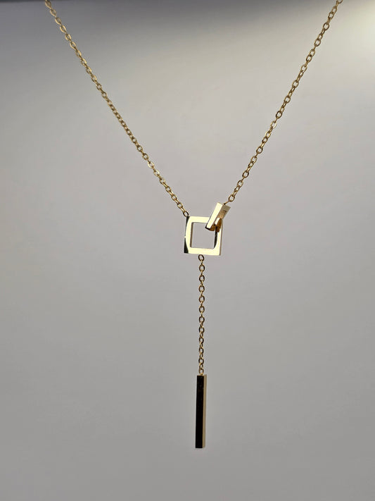 Gold necklace with a square pendant on a gray background danavi aurum