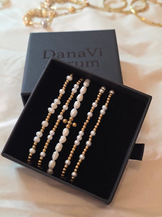 Set of pearl and gold bracelets in a Danavi aurum box on a soft fabric background